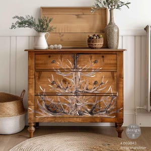 May include: A wooden dresser with four drawers, featuring a rustic design. The front of the drawers is adorned with a white antler chandelier design. The dresser is set against a white wall and a woven rug.