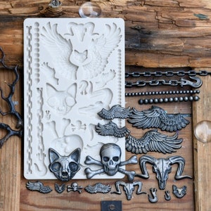 May include: A silicone mold for making resin crafts. The mold features a variety of designs, including wings, skulls, and cat heads. The mold is shown with finished resin pieces in silver.