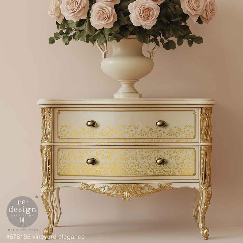 May include: A cream-colored two-drawer nightstand with gold accents and floral detailing. The drawers feature a yellow floral pattern and gold knobs. A vase of pink roses sits atop the nightstand. The text on the bottom reads "#676155 vineyard elegance".