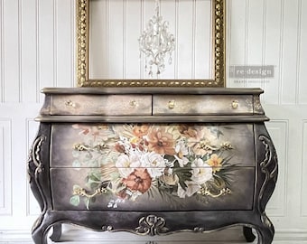 May include: A black and gold painted antique chest of drawers with a floral design. The chest has four drawers and ornate legs. The chest is decorated with gold accents and a floral design. The chest is sitting on a white wooden floor. The text "RENOVELLE BY VILMA" is on the front of the chest.