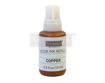May include: A small bottle of copper-colored ink refill for decorating. The bottle is labeled "re-design" and "DECOR INK REFILLS" with the color "COPPER" and the size "0.5 fl.oz (15 ml)".