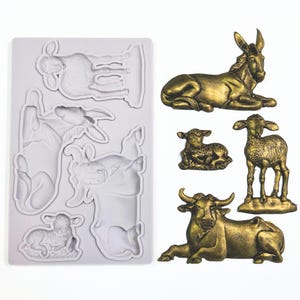 May include: A silicone mold for making edible decorations, featuring a donkey, cow, sheep, and lambs. The mold is white and the decorations are gold.