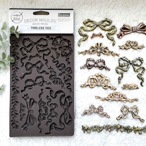 May include: A dark brown silicone mold with various bow designs and the words "DECOR MOULDS TIMELESS TIES". Several decorative bows in shades of gold, bronze, and green are displayed next to the mold. The bows vary in size and style.