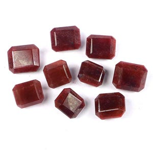 May include: A collection of eight loose, rectangular-cut gemstones with a deep, dark red colour. Each stone features faceted surfaces that reflect light, displaying a semi-translucent appearance with subtle internal variations in the red hue.