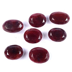 Puede incluir: Seis rubíes rojos facetados de forma ovalada dispuestos en grupo. Cada piedra preciosa presenta una superficie pulida con múltiples facetas triangulares que reflejan la luz, mostrando un color carmesí profundo y saturado en todas ellas.