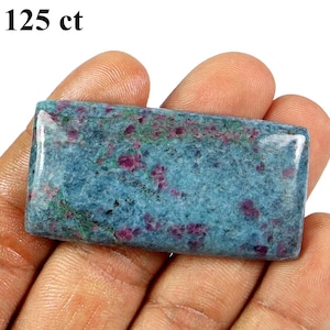 Puede incluir: Una piedra preciosa pulida rectangular con una superficie lisa, que presenta un color base azul y verde moteado con inclusiones dispersas de color rosa intenso y rojo. El texto 125 ct está impreso en la esquina superior izquierda.