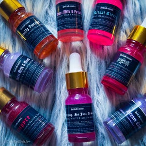 Brightly labeled vegan shimmer body oil samples on faux fur – HellaSinister mini perfume oils for layering or gifting