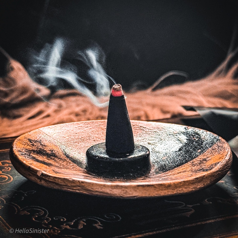 Handmade charcoal incense cones scattered beside black packaging labeled “Hollow Spirits” by HellaSinister, featuring oud, patchouli, and amber incense cones displayed on a dark gothic background.