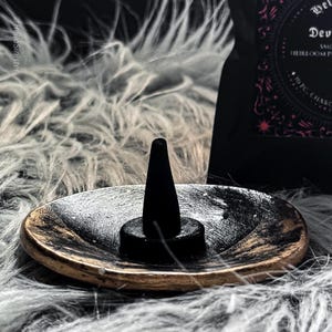 Charcoal incense cone burning on a ceramic incense holder, with a black bag labeled “Devils Croft” pumpkin and clove incense cones by HellaSinister, photographed on a dark gothic background with vintage occult book props.
