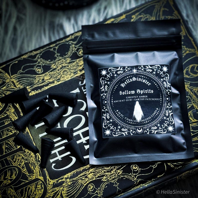 Handmade charcoal incense cones scattered beside black packaging labeled “Hollow Spirits” by HellaSinister, featuring oud, patchouli, and amber incense cones displayed on a dark gothic background.