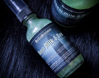 Può includere: Due bottiglie di vetro verde di olio per il corpo "Ghost Milk & Dew" con un'etichetta nera. Le bottiglie sono su una superficie scura e strutturata. L'etichetta include il marchio "BellaSinister".