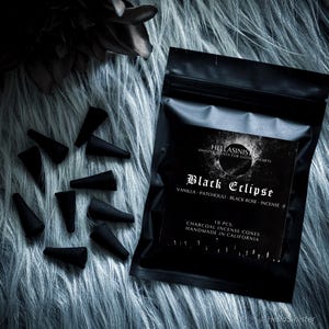 May include: Black incense cones and a black package with the text "Black Eclipse" and "Vanilla, Patchouli, Black Rose, Incense." The package also states "Charcoal Incense Cones Handmade in California."