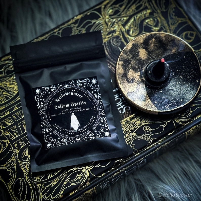 Handmade charcoal incense cones scattered beside black packaging labeled “Hollow Spirits” by HellaSinister, featuring oud, patchouli, and amber incense cones displayed on a dark gothic background.