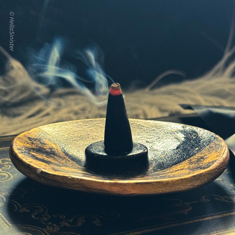 Handmade charcoal incense cones by HellaSinister displayed with packaging labeled Devils Croft, featuring a pumpkin and clove autumn incense scent, shown burning on a ceramic holder in a gothic home fragrance setup.