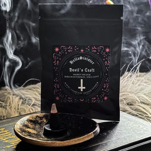 Charcoal incense cone burning on a ceramic incense holder, with a black bag labeled “Devils Croft” pumpkin and clove incense cones by HellaSinister, photographed on a dark gothic background with vintage occult book props.