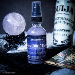 May include: A bottle of Ghost Milk & Musk body oil by HellaSinister, with a sparkling purple liquid. A crystal ball sits on a black stand, and a Ouija board and tarot card are in the background.