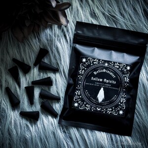 Handmade charcoal incense cones scattered beside black packaging labeled “Hollow Spirits” by HellaSinister, featuring oud, patchouli, and amber incense cones displayed on a dark gothic background.