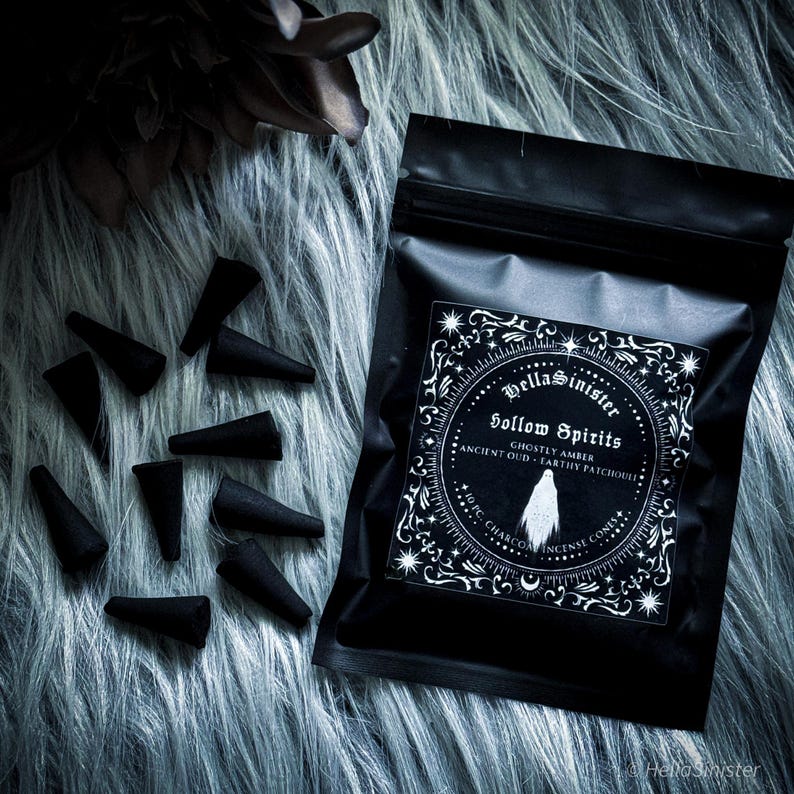 Handmade charcoal incense cones scattered beside black packaging labeled “Hollow Spirits” by HellaSinister, featuring oud, patchouli, and amber incense cones displayed on a dark gothic background.