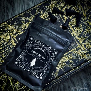 Handmade charcoal incense cones scattered beside black packaging labeled “Hollow Spirits” by HellaSinister, featuring oud, patchouli, and amber incense cones displayed on a dark gothic background.