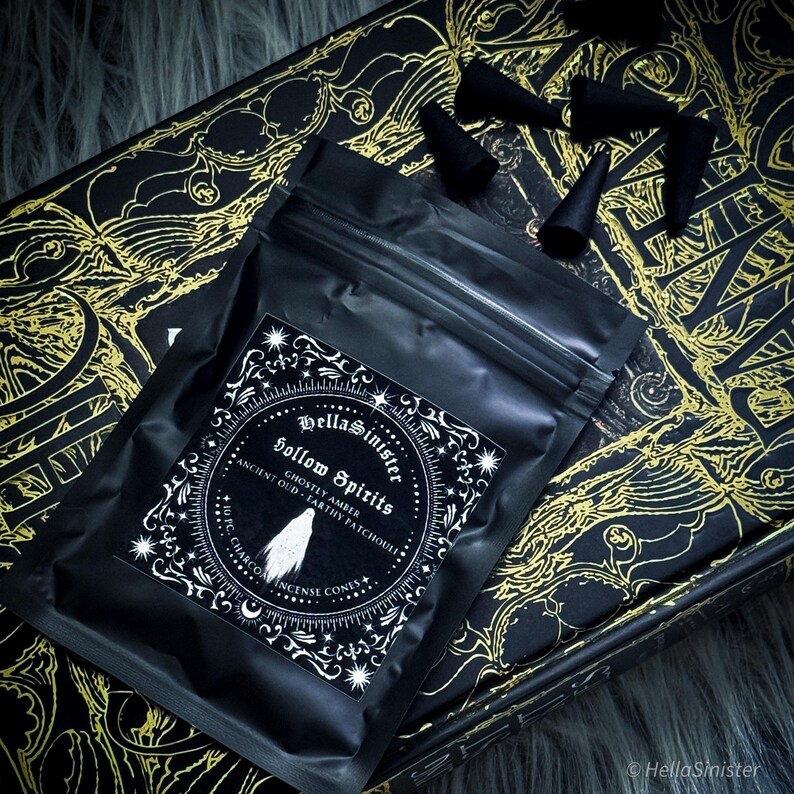 Handmade charcoal incense cones scattered beside black packaging labeled “Hollow Spirits” by HellaSinister, featuring oud, patchouli, and amber incense cones displayed on a dark gothic background.