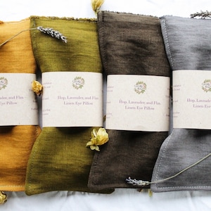Può includere: Quattro cuscini per gli occhi in lino di diversi colori: giallo senape, verde oliva, marrone e grigio. Ogni cuscino ha un'etichetta che recita "Hop, Lavender, and Flax Linen Eye Pillow".