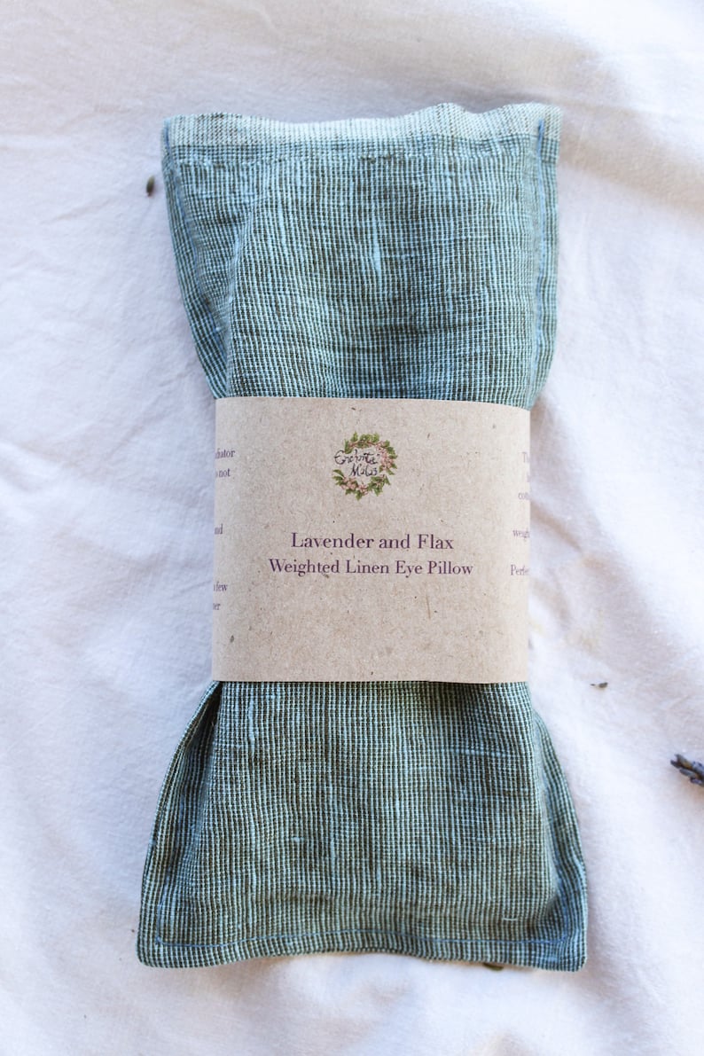 K&ouml;nnte beinhalten: Ein gr&uuml;n-wei&szlig; gestreiftes Leinen-Augenkissen mit einem braunen Papierband. Auf dem Band steht "Lavender and Flax Weighted Linen Eye Pillow". Das Kissen ist gefaltet und gebunden und liegt auf einer wei&szlig;en Oberfl&auml;che.