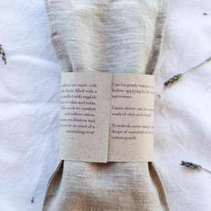 K&ouml;nnte beinhalten: Ein beiges Leinenkissen, das zur Entspannung dient, ist mit einem braunen Papierband mit Text umwickelt. Das Kissen ist mit Leinsamen und englischem Lavendel gef&uuml;llt. Der Text beschreibt die Verwendung und Pflege.