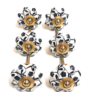 Può includere: Set di quattro pomelli per armadi in ceramica bianca con un motivo floreale nero e blu. Ogni pomello ha una base dorata e una vite.