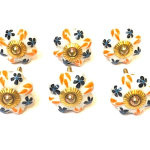 May include: Six white ceramic drawer knobs with a floral design. The knobs have a gold centre and are decorated with orange and blue flowers.