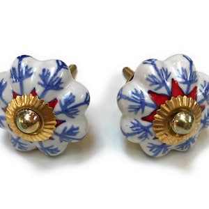 May include: Two white ceramic cabinet knobs with a floral design. The knobs have blue and red accents, and a gold-colored metal base. The knobs are designed to be used on cabinets and drawers.