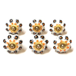 Peut inclure: Six boutons en céramique blanche avec un design en forme de coquille surélevé. Chaque bouton présente un motif floral noir et orange avec un centre doré.