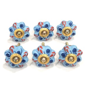 Peut inclure: Ensemble de six boutons de tiroir en céramique bleue avec un motif floral rouge et bleu. Chaque bouton a un centre doré avec un motif en relief.