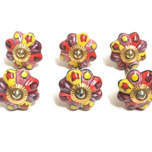 May include: Six ceramic drawer knobs with a floral design. The knobs are painted in shades of yellow, pink, red, and blue. Each knob has a gold-coloured metal centre.