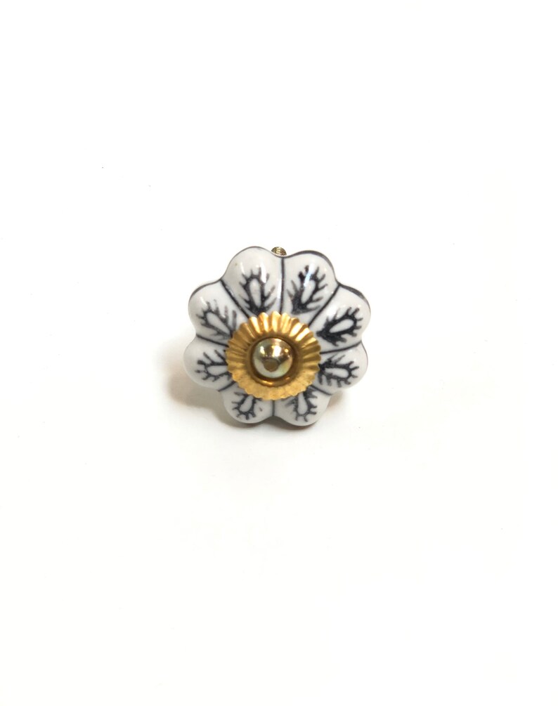以下が含まれることがあります： 黒の花柄と金色のセンターが付いた白いセラミック製のキャビネットノブ