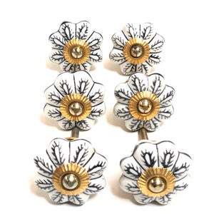 以下が含まれることがあります： 黒の花柄と金色のアクセントが付いた白いセラミック製の引き出しノブ6個セット。各ノブには取り付け用のネジが付いています。