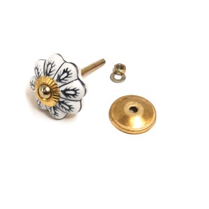 以下が含まれることがあります： 黒の花柄と金色のアクセントが付いた白いセラミックノブ。ノブには、金色のネジ、ワッシャー、ベースが付属しています。