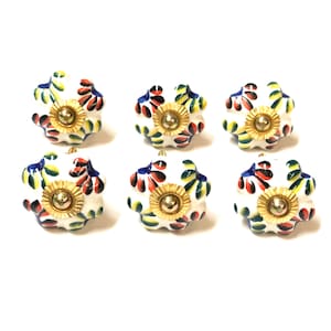 May include: Six white ceramic cabinet knobs with a floral design in shades of blue, red, yellow, and green. Each knob has a gold center.