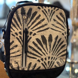 Peut inclure: Un sac à bandoulière à motif noir et blanc avec une fermeture à glissière. Le sac a une base en toile noire et une bandoulière noire.