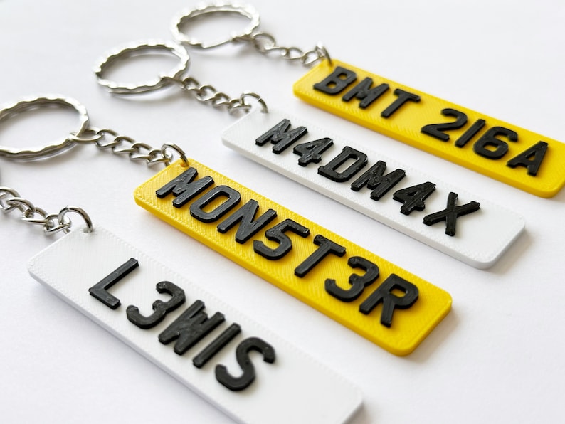 May include: Four keychains with different names printed on them. The keychains are yellow and white with black lettering. The names are "BMT 216A", "MADMAX", "MONST3R", and "L3WIS".