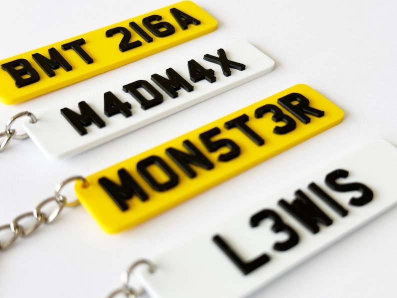 May include: Four different keychains with black lettering on white and yellow backgrounds. The keychains feature the text "BMT 216A", "M4DM4X", "MON5T3R", and "L3WIS".