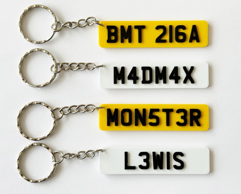 May include: Four keychains with different license plate-style tags. The tags are yellow with black lettering and read "BMT 216A", "M4DM4X", "MON5T3R", and "L3WIS".