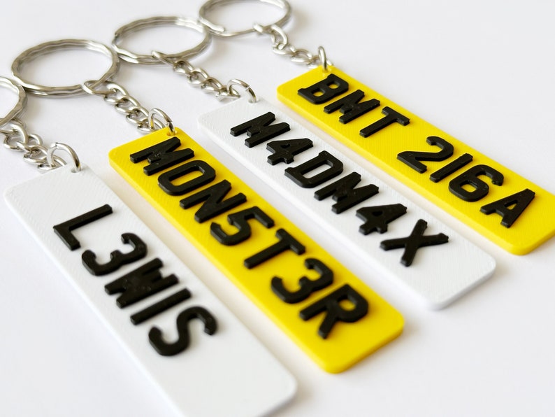 May include: Four keychains with different number plates. The keychains are yellow and white with black lettering. The number plates are "L3HIS", "MONST3R", "MADMAX", and "BMT 216A".