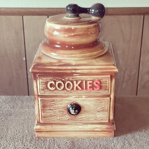 Pode incluir: Um pote de biscoitos de cerâmica marrom e branco em forma de moedor de café. O pote tem uma gaveta com a palavra "COOKIES" escrita nela.