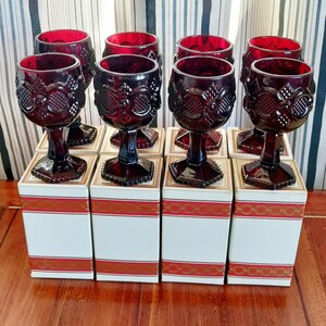 Puede incluir: Juego de ocho copas de vino rojo rubí con diseños florales y geométricos ornamentados. Las copas se exhiben sobre cajas blancas con adornos rojos y dorados. La cristalería es de vidrio y tiene una estética clásica y vintage.