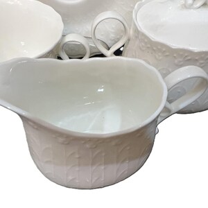 May include: A white ceramic tea set featuring a creamer, sugar bowl, and teacups. The pieces have a detailed embossed floral design and curved handles. The set is suitable for serving tea or coffee.