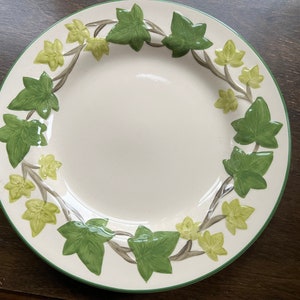 May include: A white ceramic dinner plate with a green and yellow ivy design around the rim.