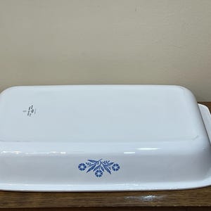 Könnte beinhalten: Weißes rechteckiges Backblech mit blauem Blumendesign. Die Schüssel hat einen leicht gebogenen Rand und einen flachen Boden. Das florale Design befindet sich an der Seite der Schüssel. Die Schüssel besteht aus einem haltbaren Material.