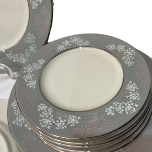 May include: A stack of gray ceramic plates with a white center and a floral pattern in white and pink. The plates have a gold rim. The plates are part of a dinnerware set.