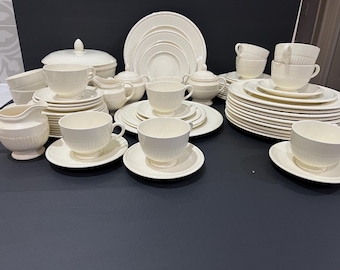 May include: A large collection of cream-colored dinnerware featuring a ribbed pattern. The set includes multiple dinner plates, salad plates, teacups with matching saucers, a lidded tureen, a creamer, a sugar bowl, and additional serving pieces.