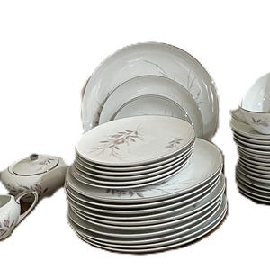 Puede incluir: Un juego de vajilla completo de porcelana blanca con un delicado diseño floral en tonos rosa y gris. El juego incluye platos, cuencos, tazas, platillos, una cremera y una azucarera, ideal para una cena formal.